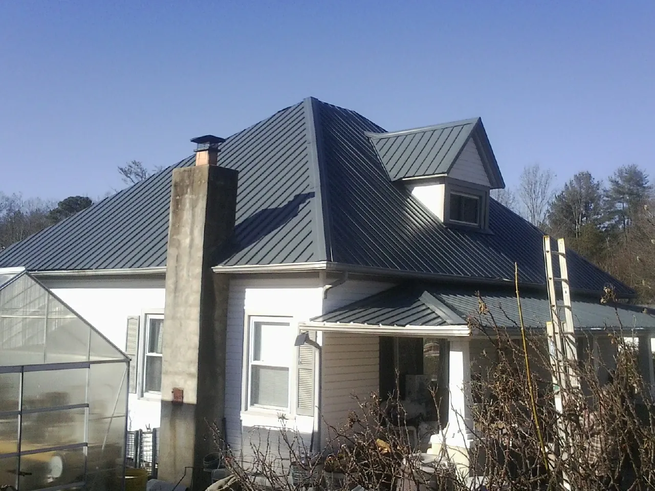 Dark blue standing seam metal roof on a white farmhouse with dormer — Slate & Tile Roof Repair by Roofing Brothers in Hallieford
