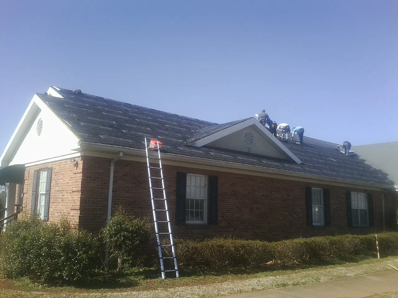 Crew tearing shingles off a brick ranch roof with a ladder set — Metal Roof Repair work by our crew in Hallieford