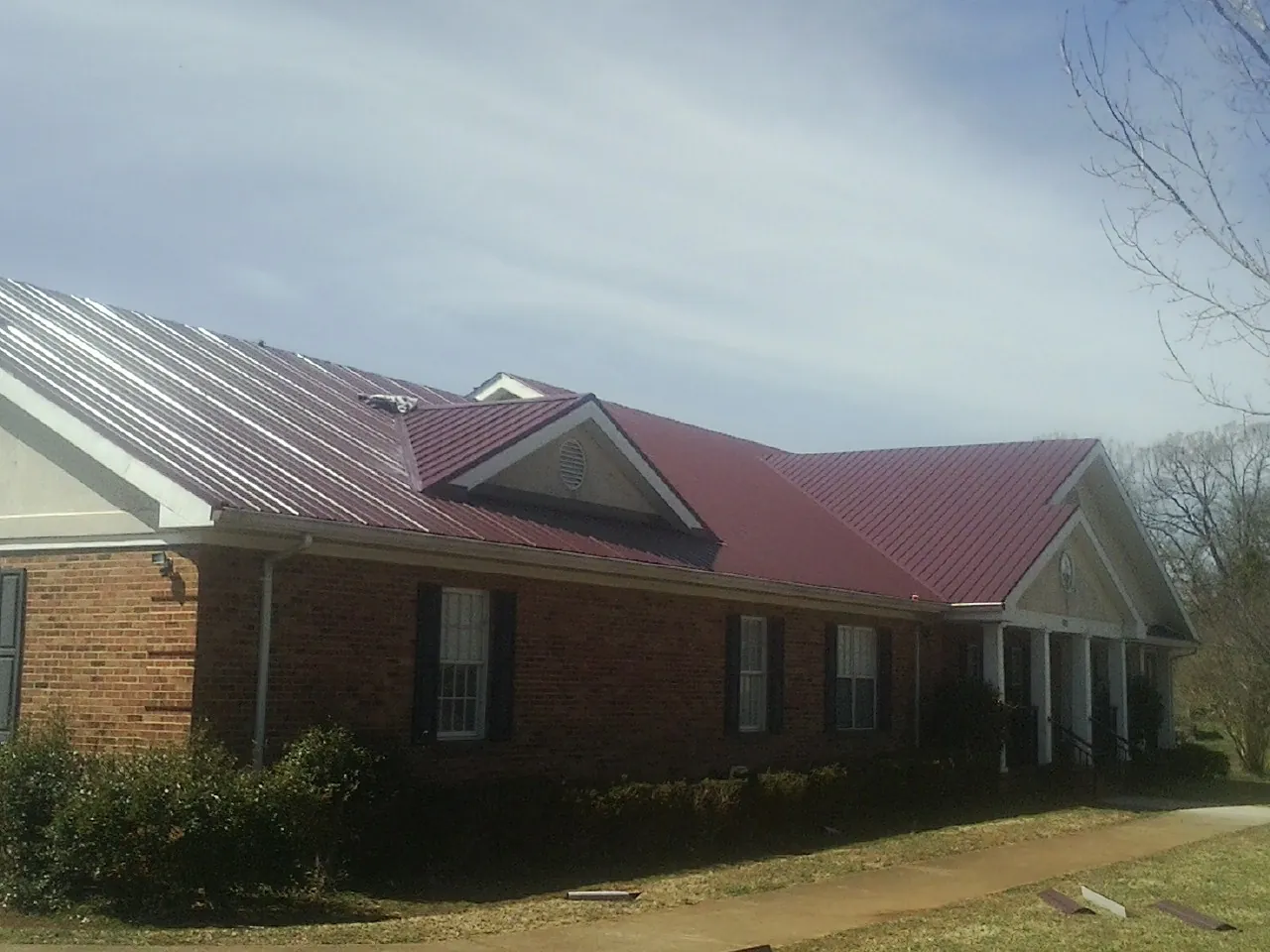 Red metal roof with gabled entries on a long brick building, from a Hail Damage Roof Repair job in Hallieford