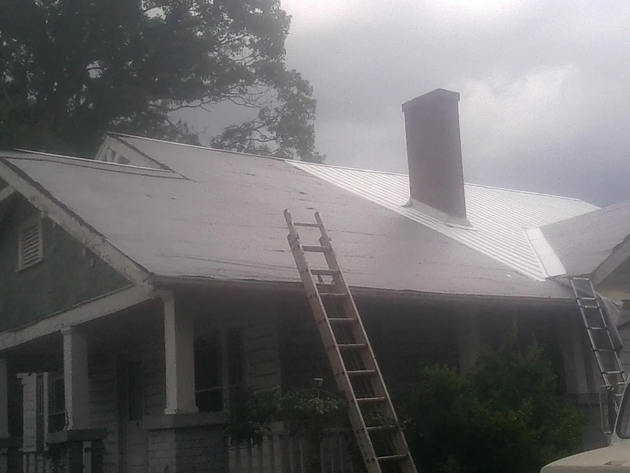 Ladders against a metal roof on an older home with a brick chimney in Hallieford