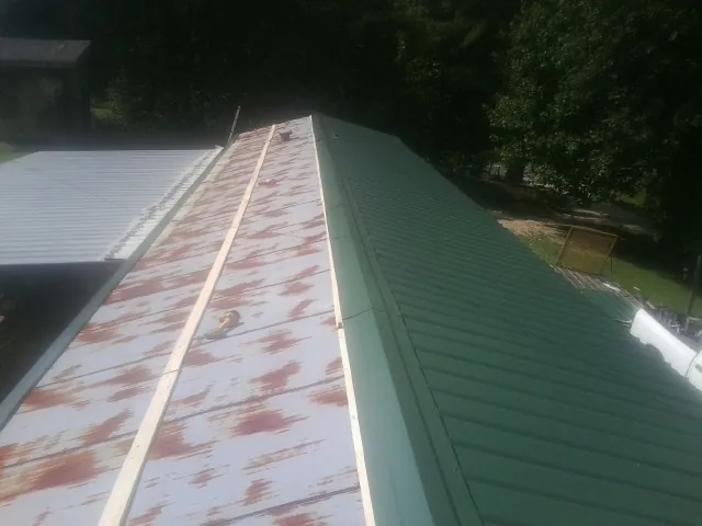 Old rusted panels beside newly installed green metal roofing — Wind Damage Roof Repair by Roofing Brothers in Hallieford