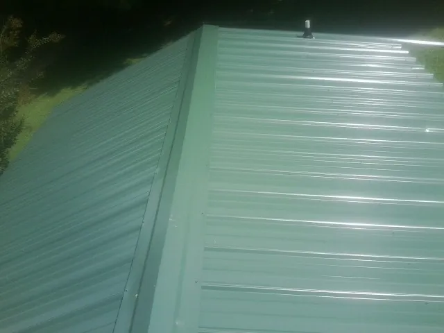 New green metal panels meeting at the ridge of a roof — Flat Roof Repair work by our crew in Hallieford