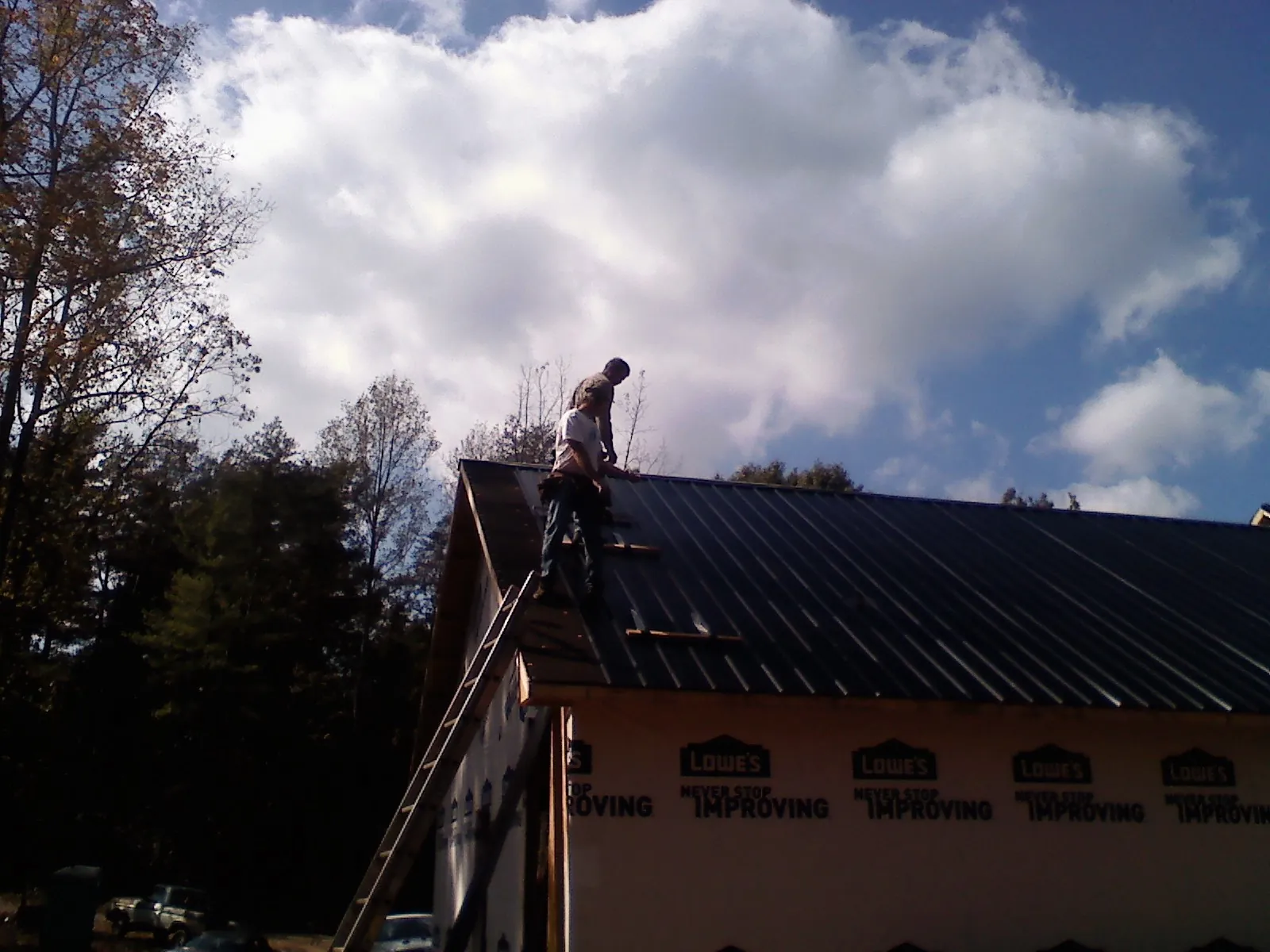 Roofer fastening dark metal panels high against a cloudy sky, from a Roof Inspection job in Hallieford