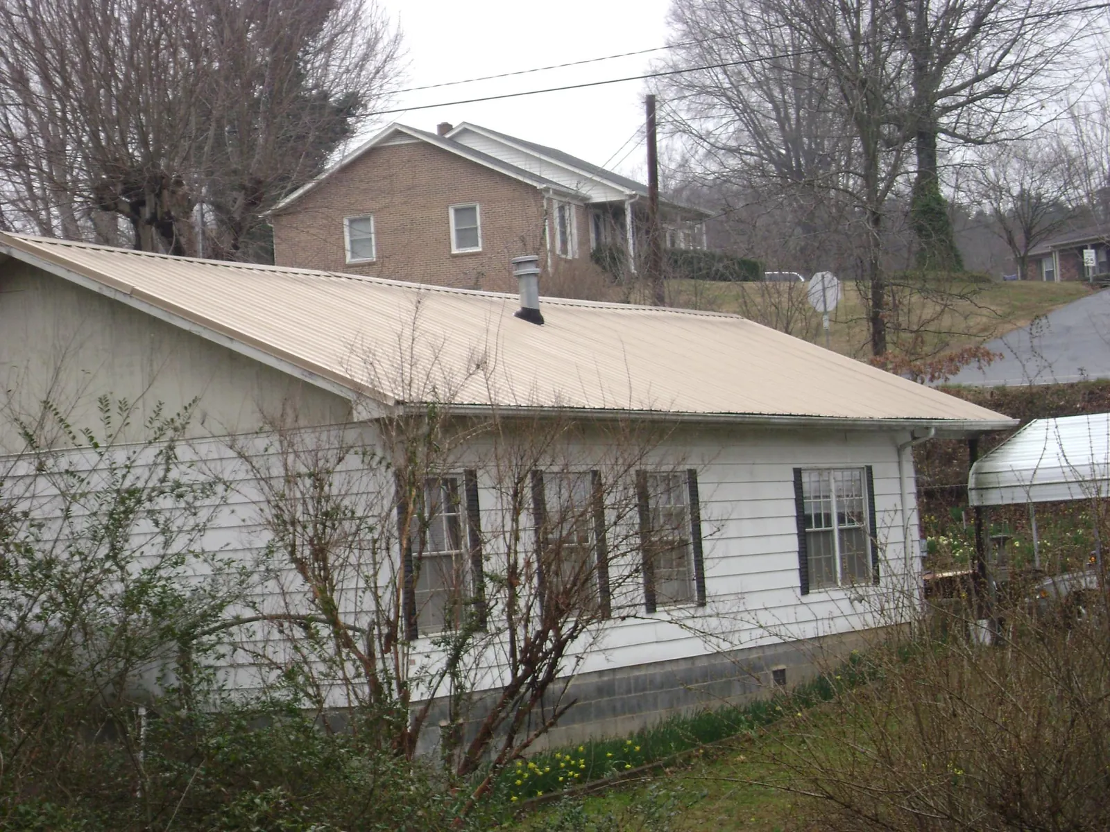 Tan metal roof on a white sided house set into a hillside — Commercial Roofing by Roofing Brothers in Hallieford